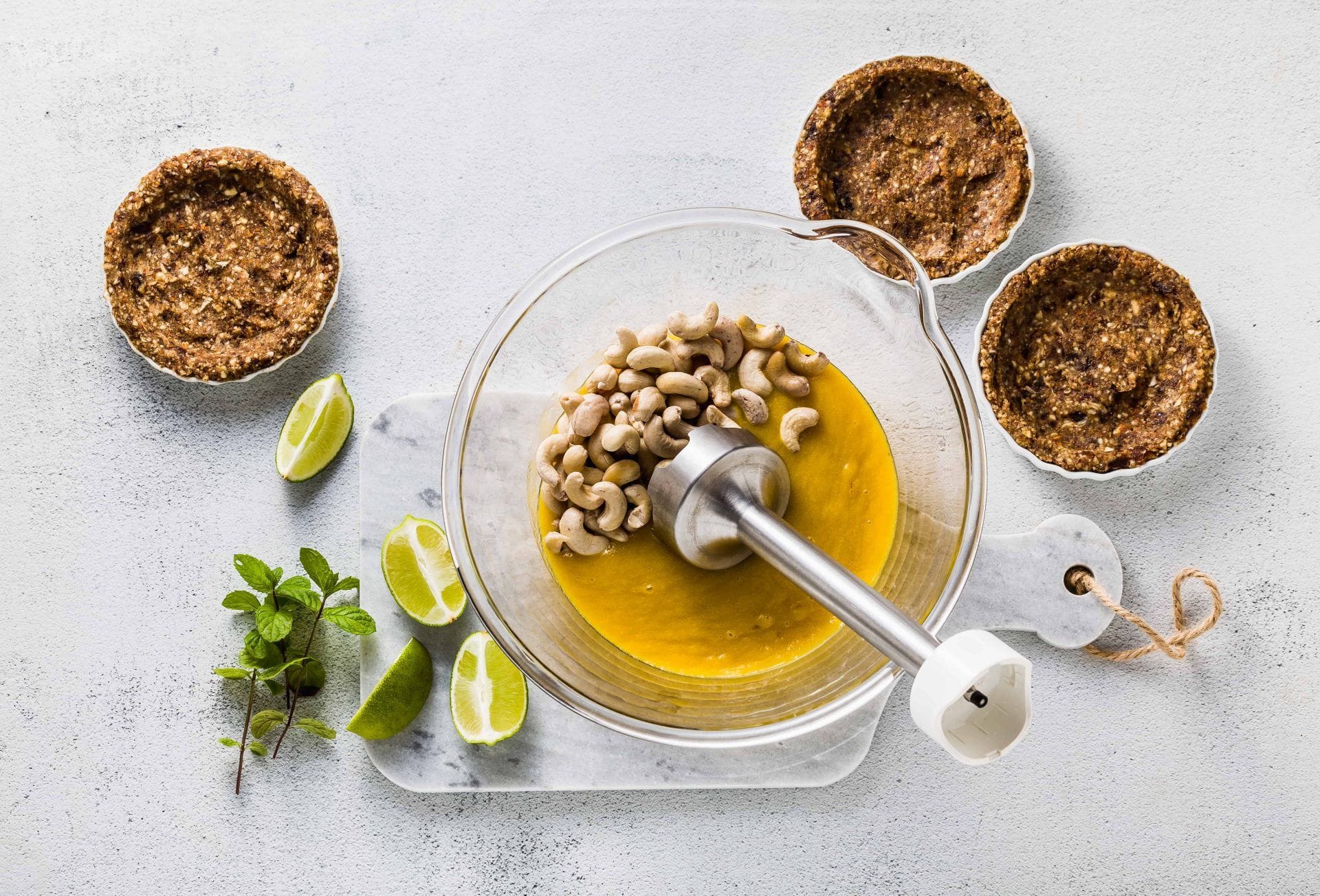 Preparation of vegan paleo cream from cashew nuts and mango puree for mini tarts made of nuts and dates with battery operated immersionblender