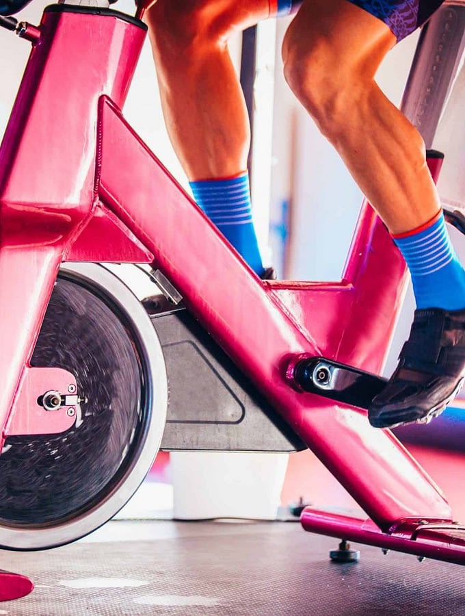 Image of a man in blue socks on a pink spin bike