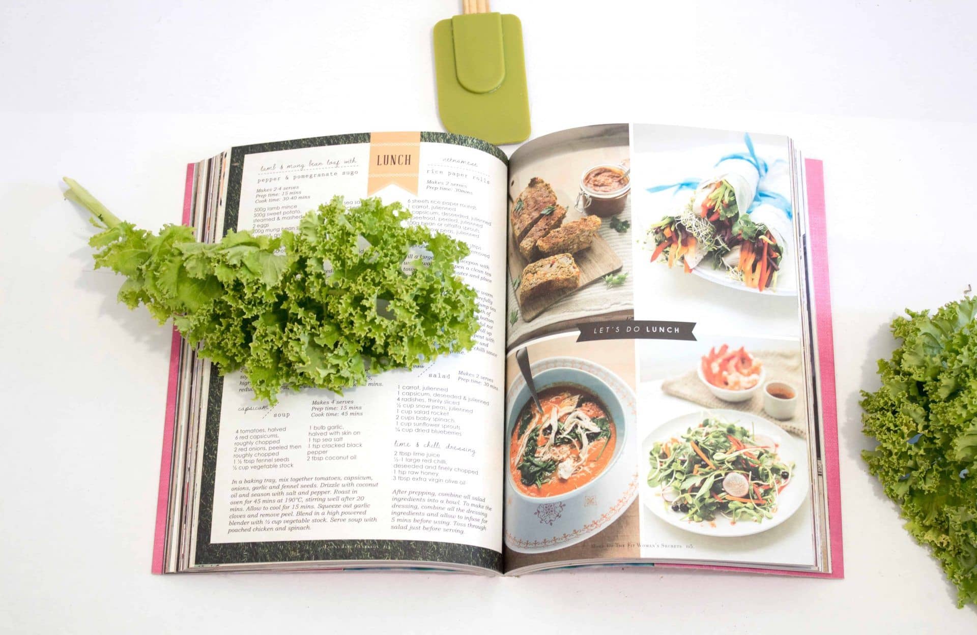 Open vegan cookbook with kale leaves and spatula next to book