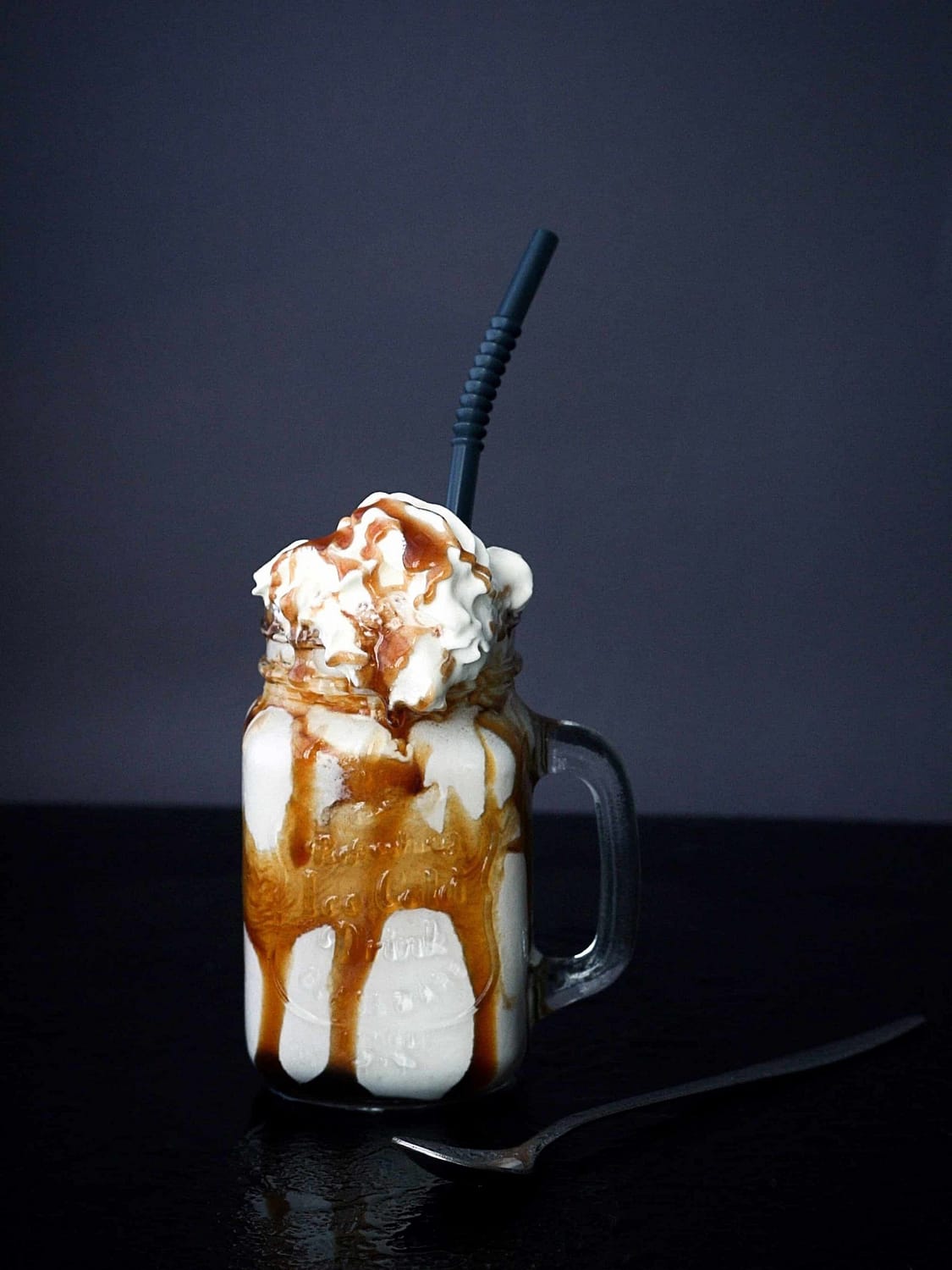 vanilla caramel milkshake in a mason jar with black straw on a black table
