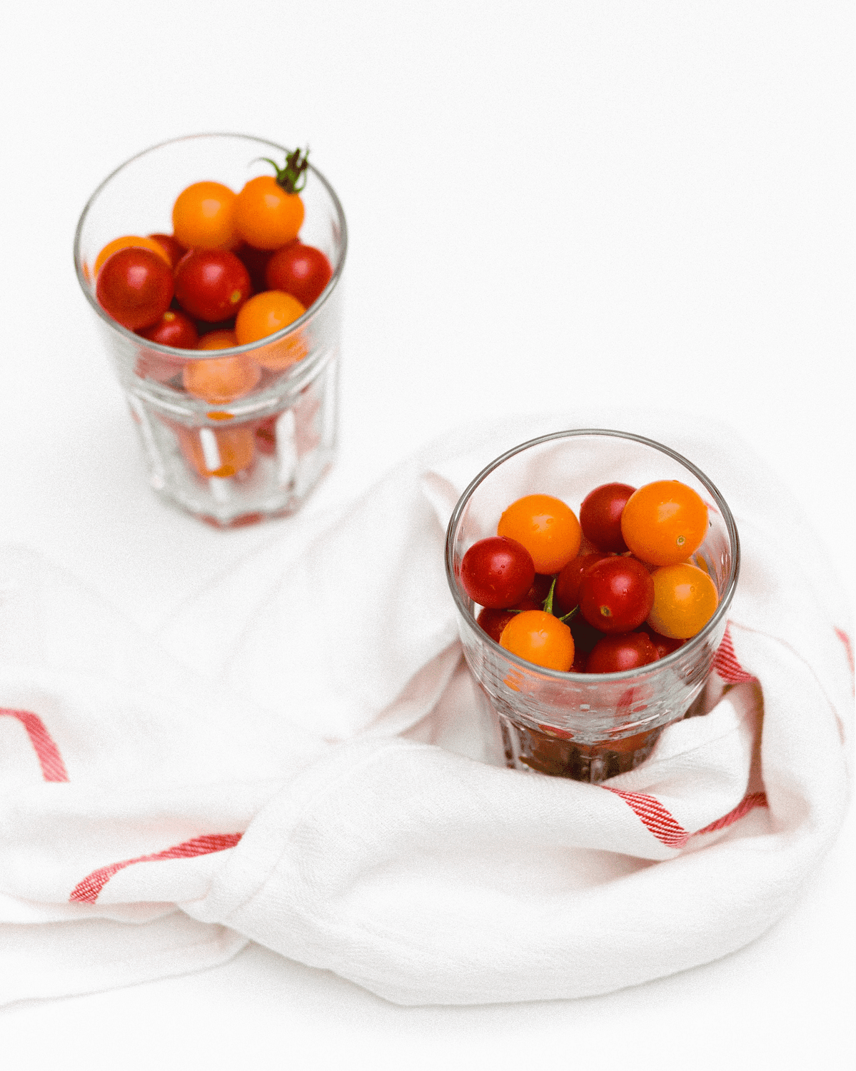 Two glass cups filled with grape tomatoes on a white table