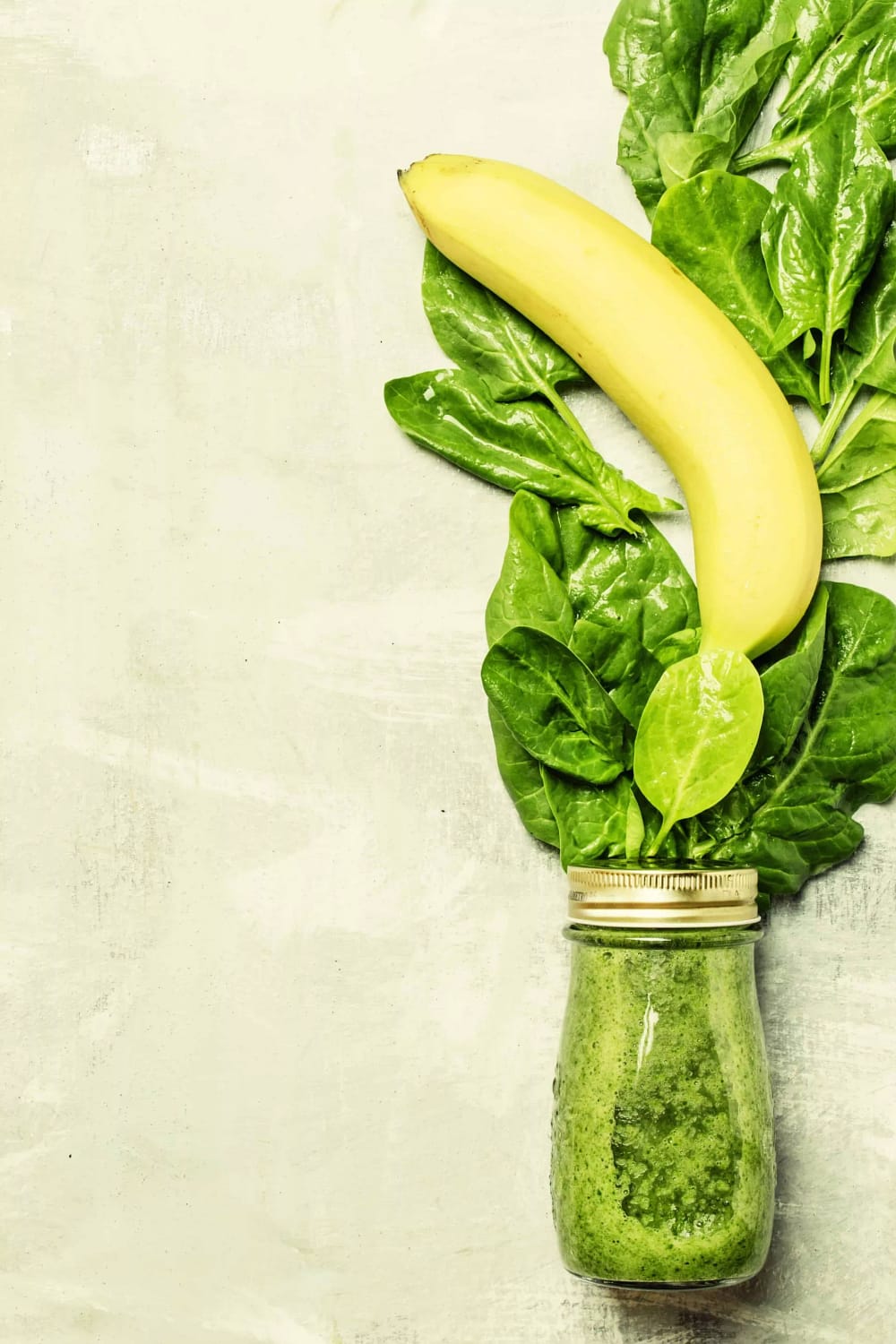 Spinach and banana green smoothies in a glass bottle, gray background