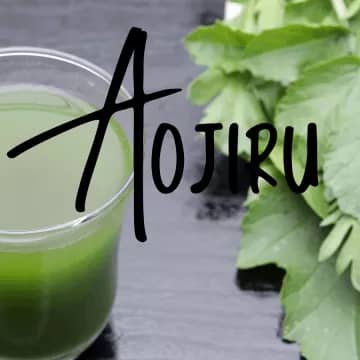 glass of aojiru juice next to green vegetables