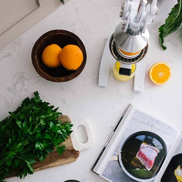 Picture of orange juicer juicing an orange next to a bowl of oranges and kale on a white countertop