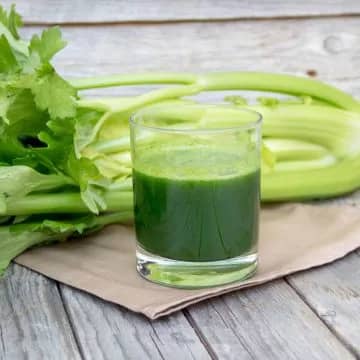 Fresh celery juice on a wooden table next to a bundle of celery